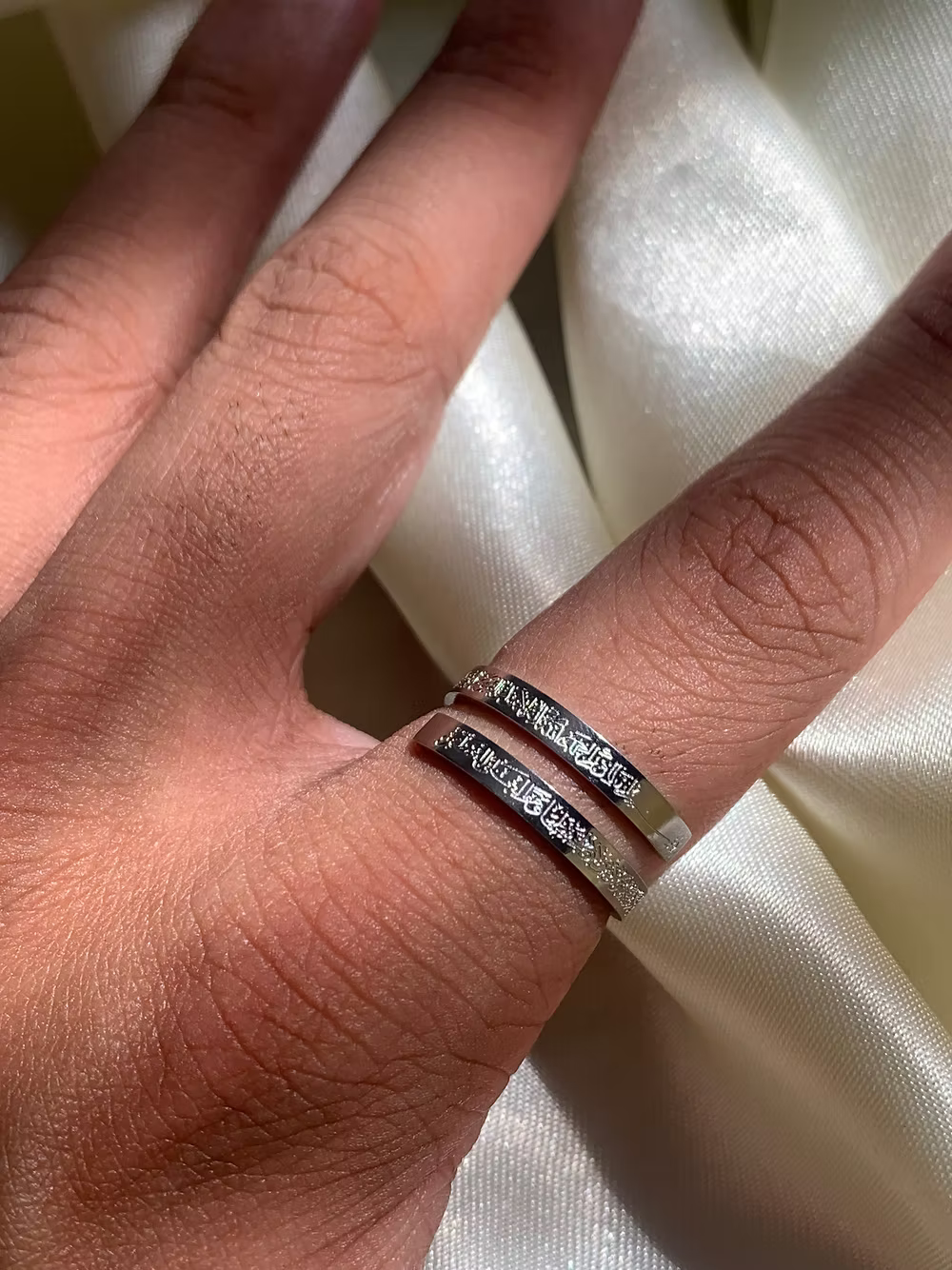 Hand wearing a silver Ayatul kursi ring with engraved text on a white fabric background