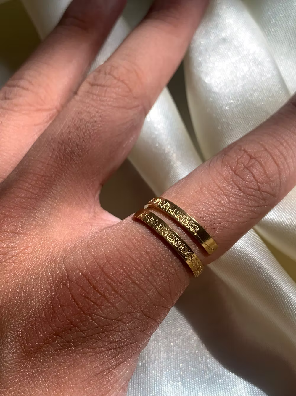 Gold Ayatul kursi ring with engraved design on a person's finger against a white fabric background