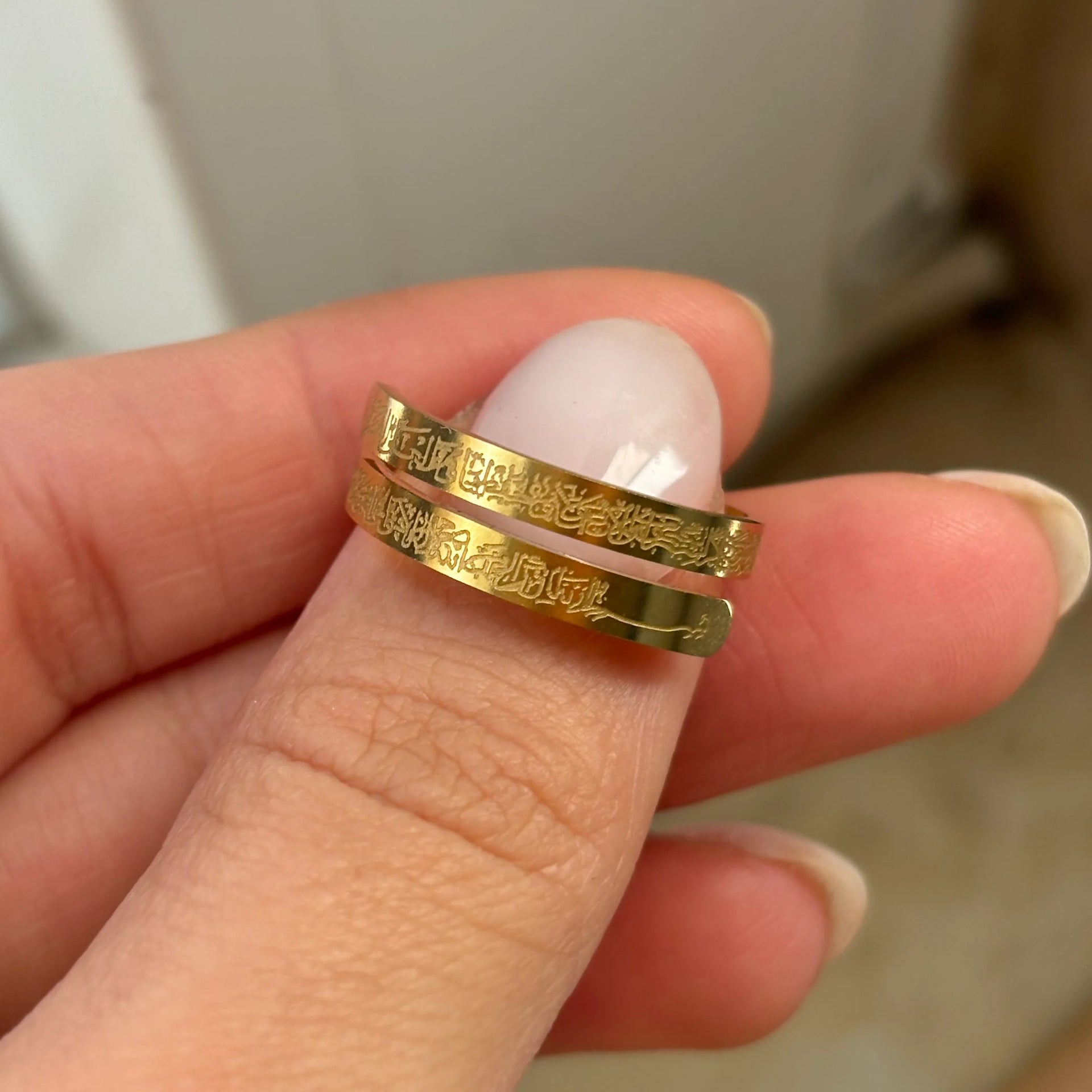 Gold rings with engraved designs held between fingers against a neutral background