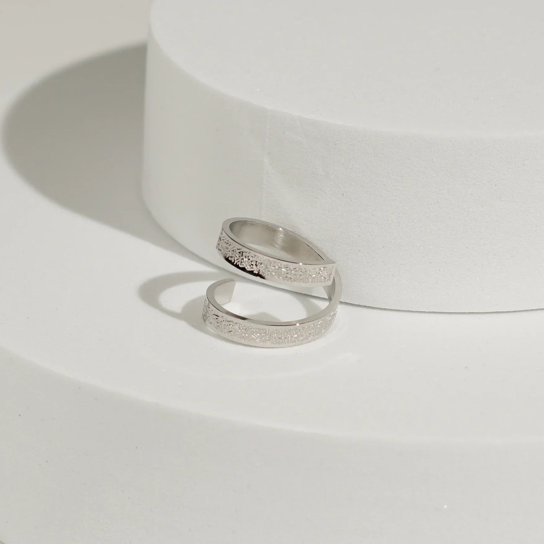 Two silver Ayatul kursi rings on a white surface with a white background