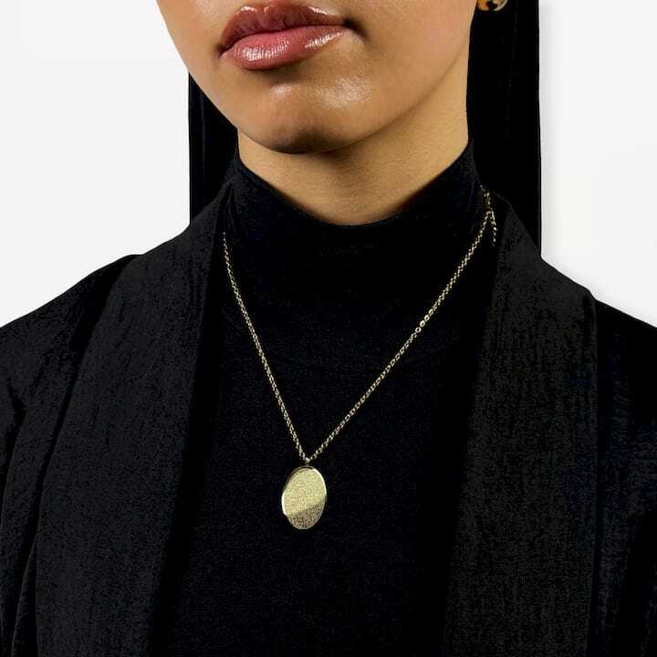 Person wearing a gold Cairo necklace with a round pendant against a neutral background