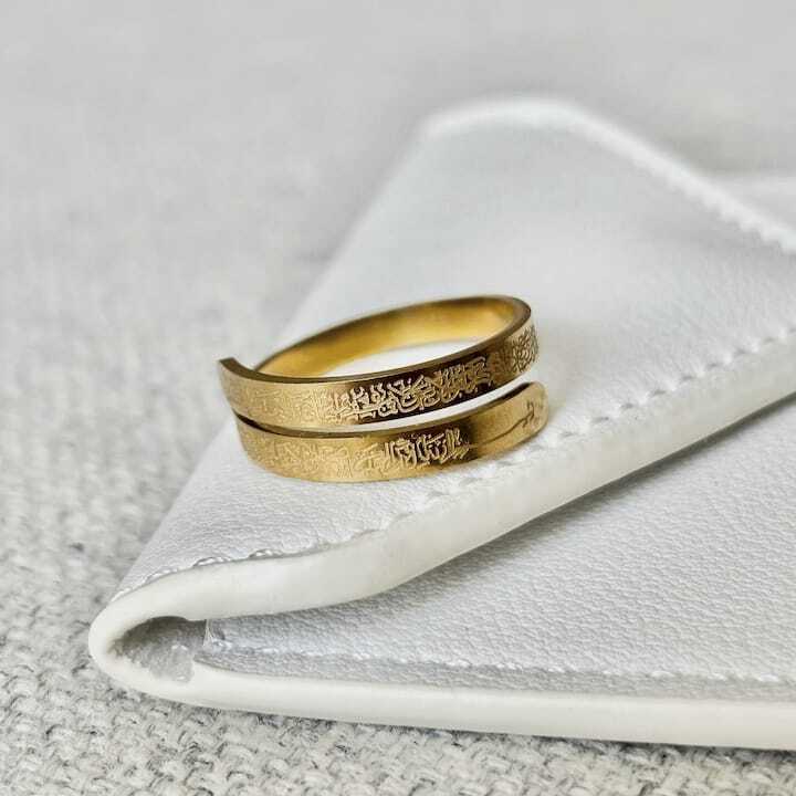 Two gold Ayatul kursi rings with engraved designs on a white fabric background