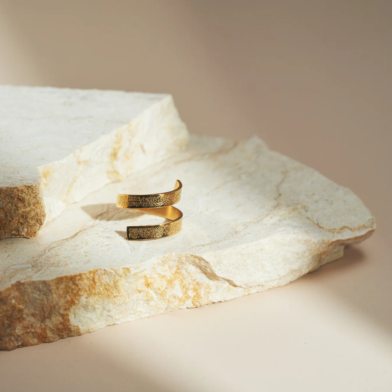 One ayatul kursi gold ring on a textured stone surface with a neutral background
