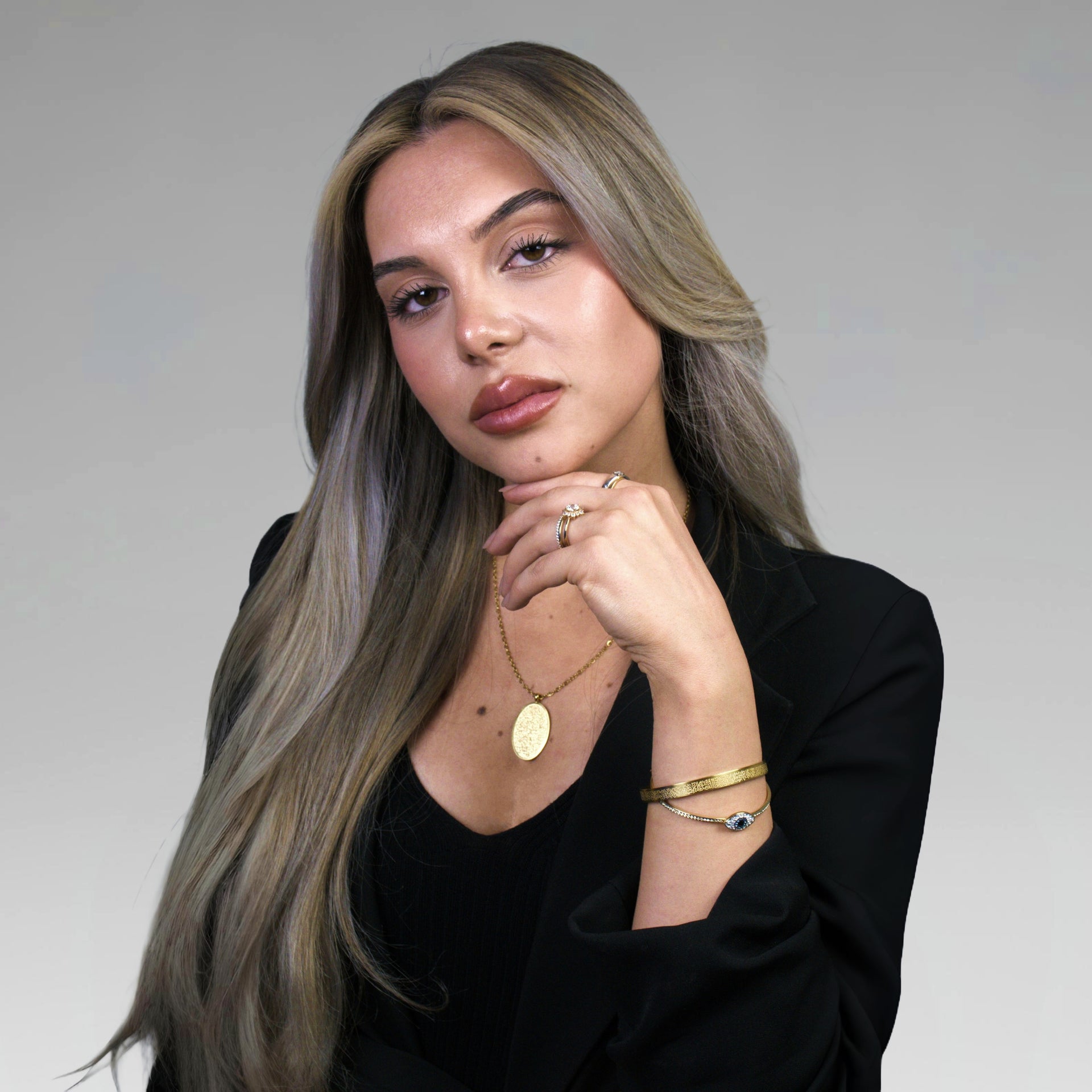 Woman with long, styled hair wearing gold jewelry against a neutral background