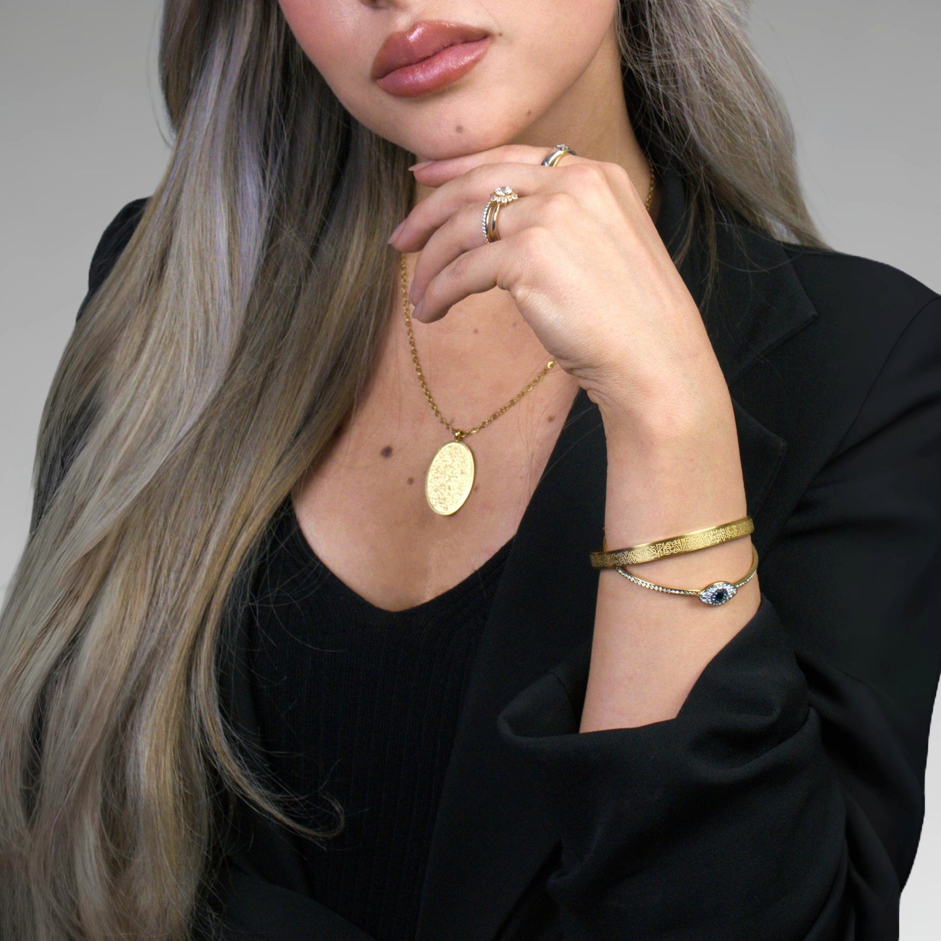 Woman wearing gold jewelry including a necklace, ring, and bracelet on a neutral background