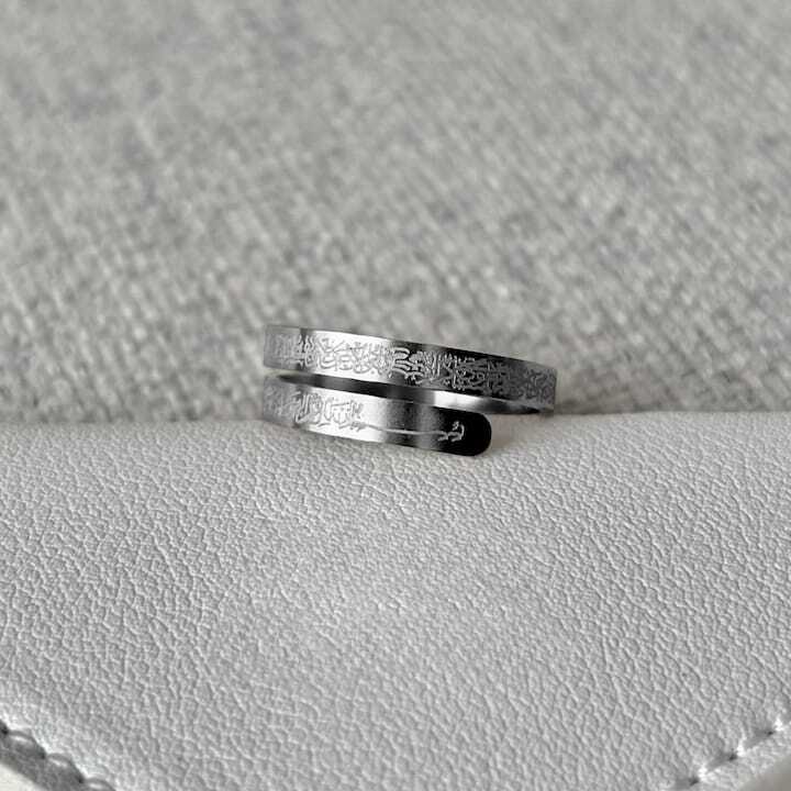 Two silver Ayatul kursi rings with engraved patterns on a textured gray surface